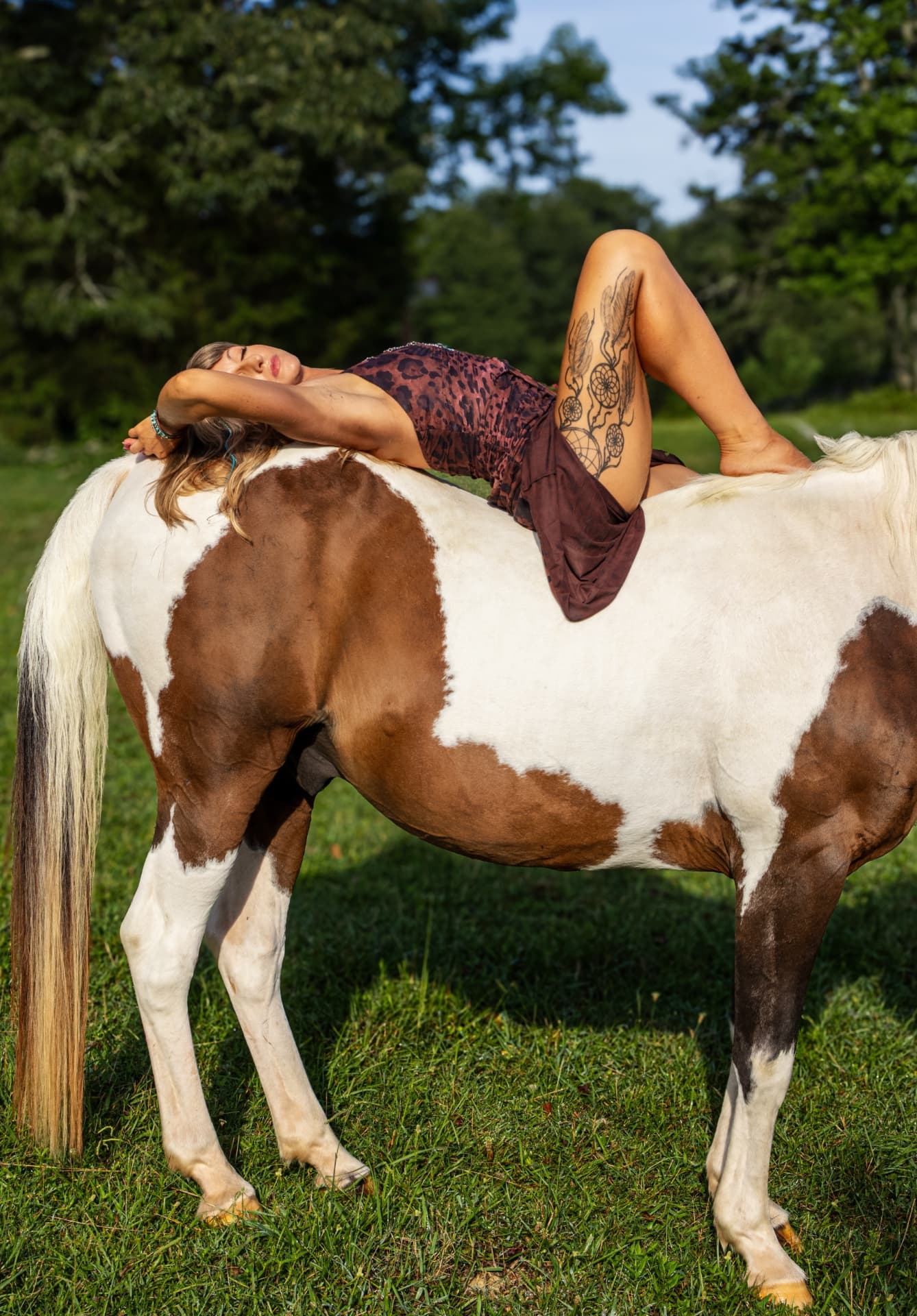 Aubree lying across her horse Wrangler, sun-kissed legs and tattoos showing a custom airbrushed glow